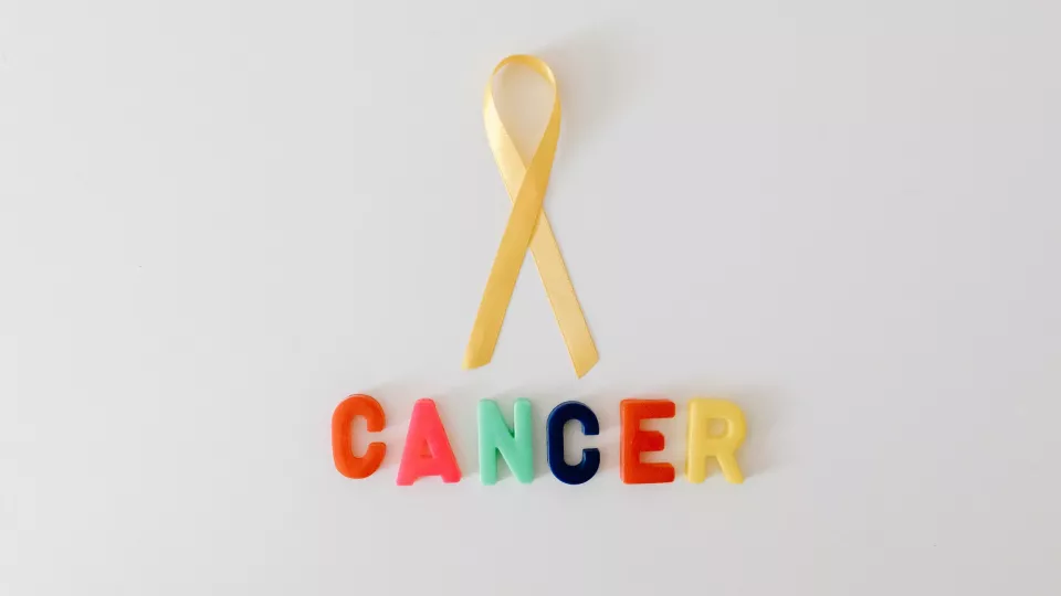 Photo of a yellow ribbon with colourful plastic letters that spell out the word cancer underneath.