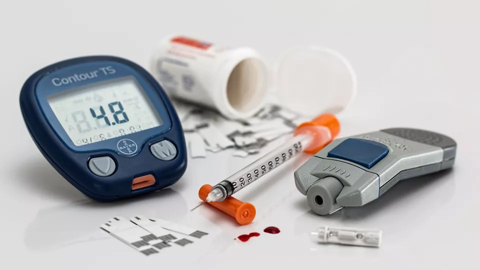 Photo of a blood glucose meter, a lancing device, an open box of pills, a syringe and 