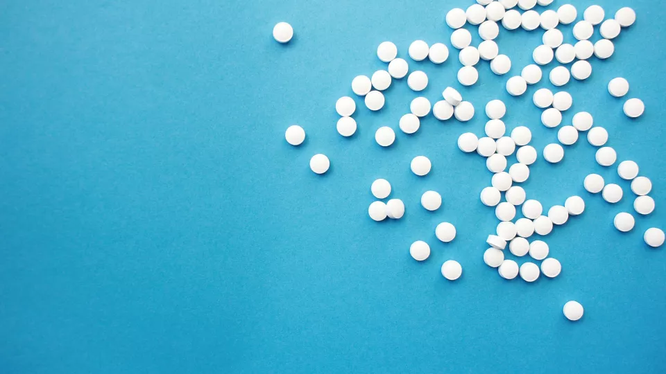 Many white small pills laying on a blue background.