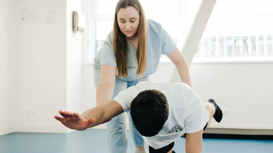 A healthcare worker who is teaching another person who's standing on his knees and hands, how to do exercises
