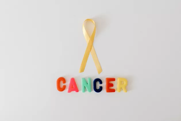 Photo of a yellow ribbon with colourful plastic letters that spell out the word cancer underneath.