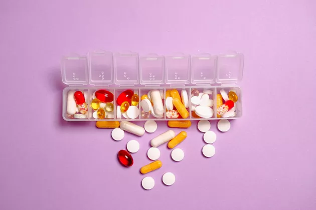 Photo of a box of different coloured pills against a pink background