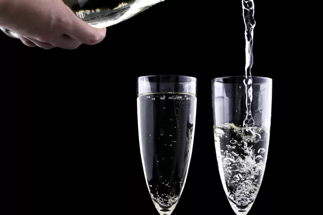 Close-up of two champagne glasses and a bottle pouring drink into one of the glasses