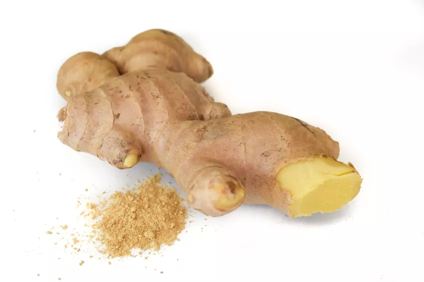 Photo of a piece of ginger next to a pile of powdered ginger against a white background.
