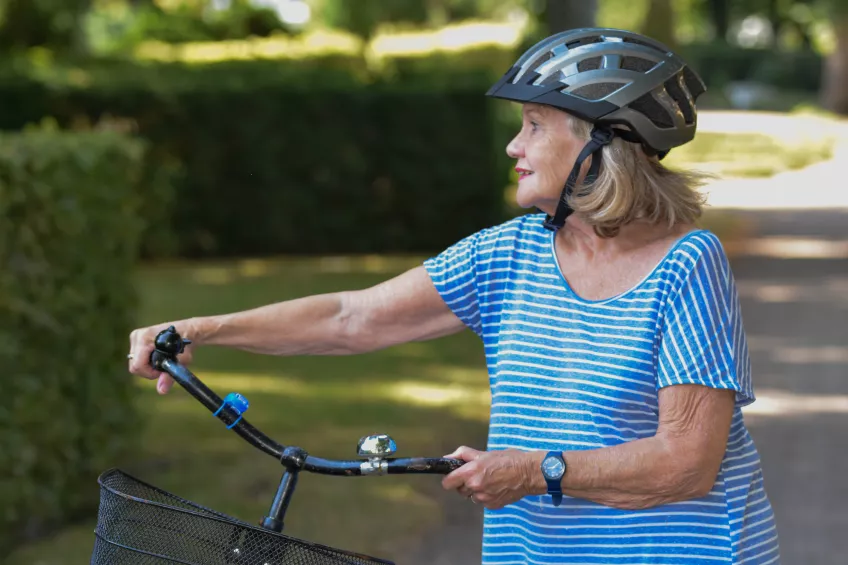 Photo of a woman in a blue and white striped t-shirt and a silver helmet holding her bike and looking to the side.