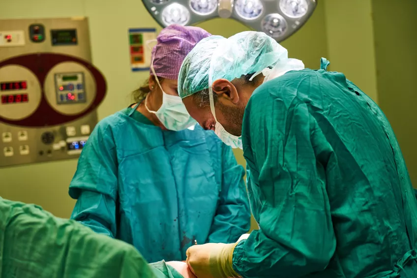 Photo of two doctors in green surgical gowns and face masks performing surgery.