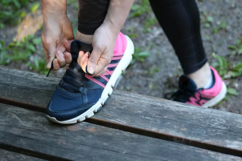 Photo of hands tying shoelaces on a blue and pink sneaker on a wooden bench.