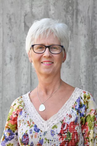 A portrait photo of Eva Ekvall Hansson. Eva is a white woman with white hair wearing glasses and a flowery top.
