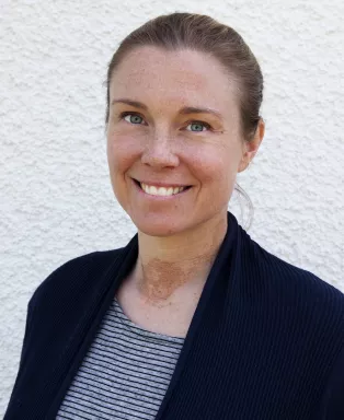 A portrait photo of Hanna Isaksson. Hanna has brown hair tied back and is wearing a striped t-shirt and a black cardigan. She is smiling.